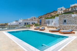a swimming pool with chaise lounge chairs next to a villa at CORFOS BLUE MYKONOS in Ornos