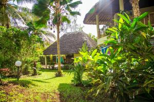 a garden in front of a house with a thatch roof at 3 Bed Cottage Sleeps 6- Pool Chef Option Parking in Diani Beach