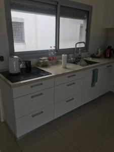 a kitchen with white cabinets and a sink and two windows at Schöne zimmer in der city tel-aviv in Karkom