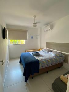 a bedroom with a bed with a blue blanket and a window at APARTAMENTO EM ARRAIAL DO CABO - RJ in Arraial do Cabo