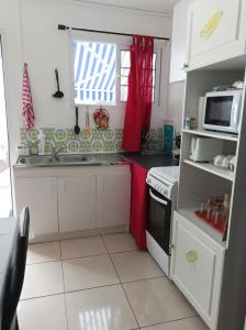 - une cuisine avec des placards blancs et un rideau rouge dans l'établissement VILLA AU COEUR DE LA MARMITE, à Sainte-Marie