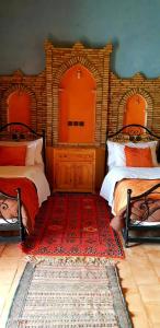 a bedroom with two beds and a red rug at Hotel Riad Le Petit Prince in Merzouga