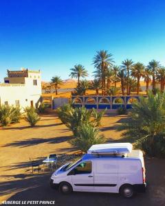 a white van parked in a parking lot with palm trees at Hotel Riad Le Petit Prince in Merzouga