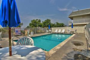 einen Pool mit Stühlen und einem blauen Sonnenschirm in der Unterkunft Motel 6-Sacramento, CA - South Sacramento and Elk Grove in Sacramento