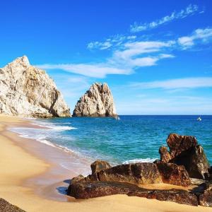 una playa con rocas en el agua y el océano en Hotel Colonos Los Cabos en Cabo San Lucas