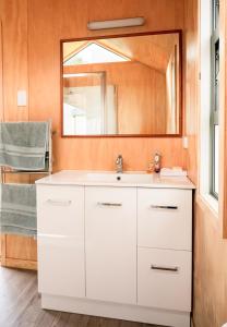 W łazience znajduje się biała umywalka i lustro. w obiekcie The Quarters Ocean-View Chalet w mieście Gisborne