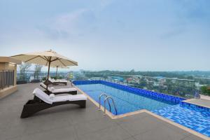 a swimming pool with chairs and an umbrella next to a pool at Ginger Kochi, Kalamassery in Cochin