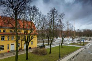 un groupe d'arbres devant un bâtiment jaune dans l'établissement Apartamentai prie Meriadiano, à Klaipėda