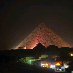 a pyramid is lit up at night in front at Maged Pyramids View Inn in Cairo