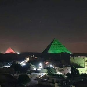 a green lighted pyramid in a city at night at Maged Pyramids View Inn in Cairo
