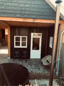 een gebouw met een witte deur en twee stoelen bij Tiny House Thuus in Sint Annaland