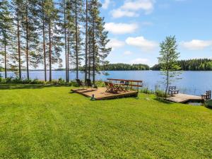 a picnic table and benches on a lawn near a lake at Holiday Home Villa niemi by Interhome in Kotalahti