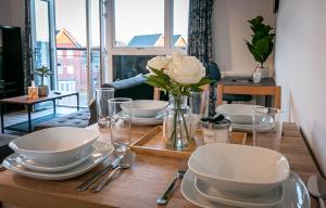 uma mesa de madeira com pratos e tigelas e um vaso de flores em Aryas Apartments Milton Keynes em Broughton