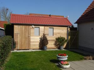 a wooden building with a red roof in a yard at Kustverhuur, Park Schoneveld, Stern 234 met eigen elektrische laadpaal in Breskens