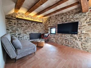 - un salon avec un mur en pierre, un canapé et une télévision dans l'établissement Cal Serni, à Calbinyà