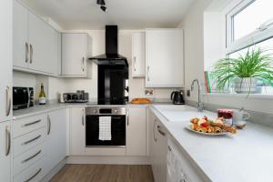 Lawsons Place - Family-Friendly Apartment with Parking on Babbacombe Downs in Torquay في توركواي: مطبخ مع خزائن بيضاء وطبق من الطعام على المنضدة