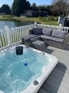 bañera de hidromasaje en una terraza junto a un sofá en Lakeside Retreat Lodge With Hot Tub en Pocklington