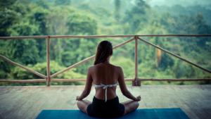 a woman sitting on a yoga mat looking out at the forest at Big Tree Cottages in Beadonābād