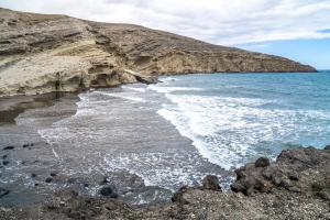 a beach with rocks and water and a mountain at Casa la Sonrisa shared house in El Médano