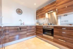 uma cozinha com armários de madeira e um relógio na parede em Amber Apartment Oasis - Your Gateway to Southampton's Vibrant Heart, Port, Shopping em Southampton