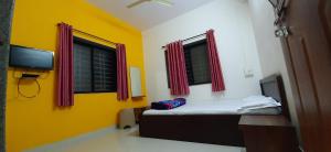 a room with a bed with yellow walls and windows at Trimurti Holiday Home in Panchgani