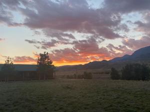 un coucher de soleil dans un champ avec une grange et des montagnes dans l'établissement Yellowstone Cutthroat Guest Ranch, à Wapiti
