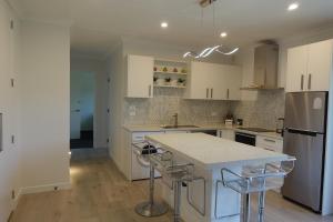 a kitchen with white cabinets and a island with bar stools at The Guest House in Tamahere