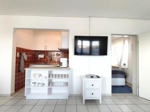 a kitchen with white cabinets and a tv on a wall at Ferienwohnung am Deich in Friedrichskoog