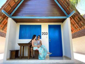 two women sitting on a bench in front of a blue door at Tijota Hotel Fazenda in Ipatinga