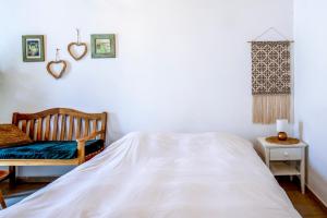 a white bedroom with a bed and a chair at רז אירוח ברמה in Qasrîne