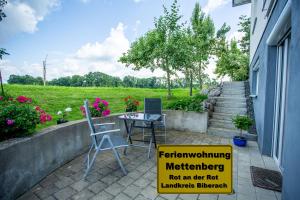 znak siedzący na patio ze stołem i krzesłami w obiekcie Ferienwohnung Mettenberg w mieście Rot an der Rot