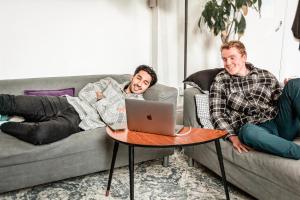 two men laying on a couch with a laptop on a table at Urbany Hostel London 18-40 Years Old in London