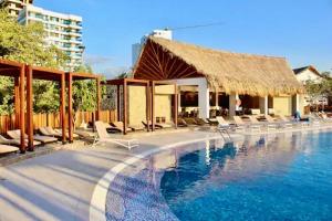 una piscina con sillas y un edificio con techo de paja en Preciosos Apartamentos en Samaria Club de Playa sector Pozos Colorados, en Santa Marta