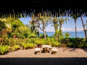 a picnic table and benches on a beach with the ocean at Copa De Arbol Beach & Rainforest Resort in Drake