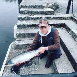 a man sitting on steps holding a fish at Ryan's River Lodge B&B in Cong