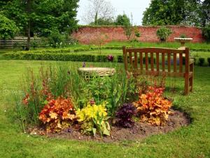 un jardín con un banco y flores en el césped en Broomhouse Farmhouse, en Cheswick