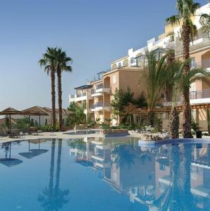 a large swimming pool with palm trees and a building at Aphrodite Springs in Paphos City