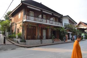 a man in an orange robe walking past a building at Sala Prabang Hotel in Luang Prabang
