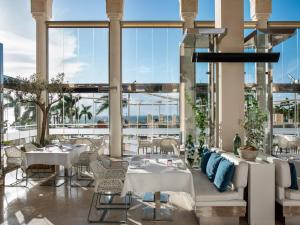 un restaurante con mesas y sillas blancas y ventanas grandes en Gran Melia Palacio de Isora Resort & Spa en Alcalá
