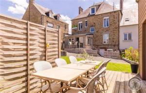 eine Terrasse mit Tisch und Stühlen auf einem Deck in der Unterkunft Maison charmante à Pontorson avec piscine partagée in Pontorson