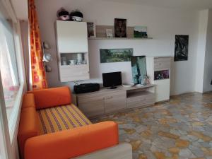 sala de estar con sofá naranja y TV en Punta Ala Top apartment, en Punta Ala