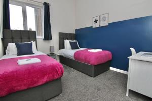 a bedroom with two beds with pink sheets and a blue wall at Mount Haven's Rest - Free Parking, Netflix & Private Back Garden in Coventry