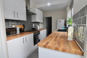 une cuisine avec des placards blancs et un comptoir en bois dans l'établissement Stylish 4Bed Retreat - Walk to Coventry's Delights, à Coventry