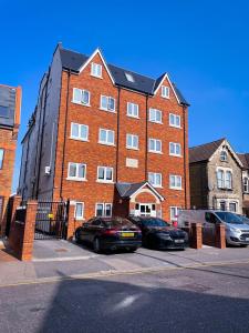 un gran edificio de ladrillo con coches aparcados en un aparcamiento en Ilford Luxury Apartments en Ilford