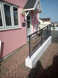 een roze huis met een zwarte leuning naast een deur bij The Pink House, Paignton in Paignton