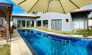 a swimming pool with an umbrella in front of a house at 6 suítes Búzios frente Mar ! Piscina , casa NOVA in Búzios