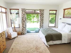 a bedroom with a bed and a chair and windows at River View Escape close to Mount Maunganui & shops in Tauranga