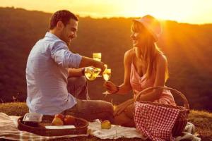 Un uomo e una donna che bevono vino mentre sono seduti su una coperta da picnic di Eildon Parkview Motor Inn Room 11 a Eildon