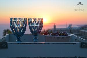 due bicchieri da vino seduti su un tavolo con una ciotola d'uva di Pyrgos Houses and Restaurant ad Avgónyma