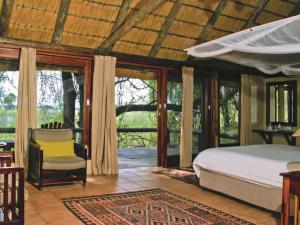 a bedroom with a bed and a chair and windows at Lianshulu Lodge in Kongola